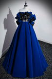 Blue evening gown with black floral details on a mannequin against a white wall.