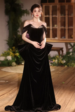 Woman in a black off-shoulder gown standing indoors with decorative background