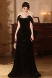 Woman in a black evening gown standing in a dimly lit room with a piano.