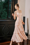 Woman in a pink evening gown standing indoors with a window and chair in the background.