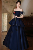 Woman in a dark blue off-shoulder gown with floral details in an indoor setting.