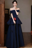 Woman in a navy blue off-shoulder gown holding a red flower indoors.