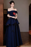 Woman in a dark blue off-shoulder gown holding a red rose indoors.