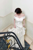 Woman in a white off-shoulder dress standing on a staircase.