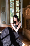 Woman in a black dress sitting in a room with ornate decor and large windows.