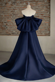 Navy blue evening gown with a large bow on a mannequin against a brick wall.