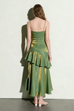 Woman wearing a green satin dress with ruffled layers against a white wall.
