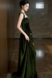 Woman in a green velvet gown standing against a dark marble wall.