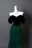 Mannequin wearing a black velvet top and green feathered skirt against a gray background