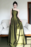 Woman wearing a green one-shoulder dress standing in a room with a white couch.