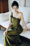 Woman in a green dress sitting on a white couch in a well-lit room.