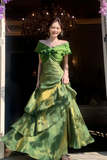 Woman in a green evening gown standing in a dimly lit room with a chandelier.