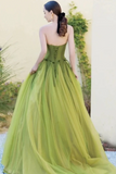 Woman in a green strapless gown standing outdoors with plants in the background