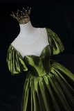 Green satin gown on a mannequin with a gold crown against a black background