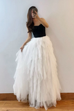 Woman wearing a black top and white tulle skirt against a plain wall.