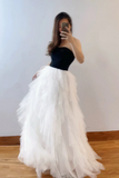 Person wearing a black top and white tulle skirt in a room with a plain wall.