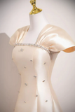 Mannequin wearing a beige evening gown with crystal embellishments on a plain background