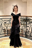 Woman in a black evening gown standing in an elegant interior setting.