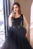Woman in a black evening gown holding a glass, standing in a softly lit room.
