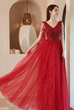 Woman in a red evening gown with beaded details standing in an elegant interior setting.