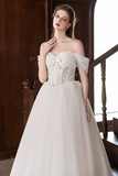 Woman wearing a white wedding dress with floral details in an indoor setting.