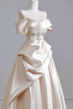 White off-shoulder evening gown with a decorative waistband on a mannequin against a gray background.