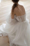 Woman wearing a white dress with sheer overlay in a softly lit room.