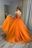 Woman wearing an orange evening gown with a sheer overlay in a room.