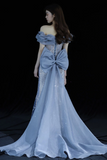Woman wearing a light blue evening gown with a large bow detail on a black background
