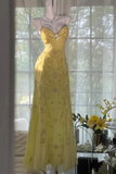 Yellow evening gown on a mannequin in front of a window with a view of trees.