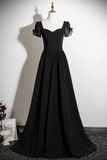 A floor-length black formal gown displayed on a mannequin against a plain white wall. The dress has sheer puff sleeves with black lace inserts, a fitted bodice, and a full skirt.
