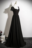 A floor-length black evening gown displayed on a mannequin against a white wall. The dress has sheer puff sleeves, a fitted bodice, and a full skirt, with a gold mannequin stand visible at the top.