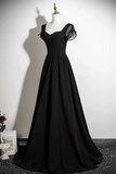 A floor-length black formal gown displayed on a mannequin against a plain white wall. The dress has a fitted bodice, a full skirt, and sheer puff sleeves with black ribbon ties at the shoulders.