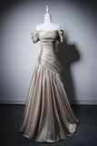 An elegant off-the-shoulder evening gown in a champagne satin fabric, displayed on a white mannequin against a dark gray studio background.