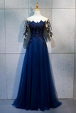 A floor-length navy blue evening gown displayed on a mannequin against a light gray tiled wall. The dress has a fitted embellished bodice, off-the-shoulder lace sleeves, and a flowing tulle skirt.