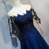 A navy blue formal gown displayed on a cream mannequin torso. The dress features a sweetheart neckline, a strapless fitted bodice, and three-quarter sheer sleeves heavily decorated with matching navy blue floral lace appliques and sequins.
