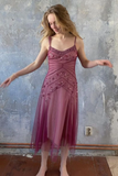 Woman in a pink dress with intricate detailing against a textured wall.