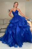 A woman wearing a royal blue strapless ball gown with a ruffled tulle skirt, standing in a living room and holding a light blue clutch.