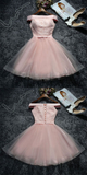 A light pink off-the-shoulder tulle dress is shown from both front and back in a flat-lay arrangement on a dark textured background, with shoes, flowers, and magazines placed around it.