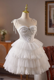 A white tiered tulle dress with a lace-up sweetheart bodice and thin shoulder ties, displayed on a cream mannequin in an indoor room setting.