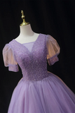 A lavender purple ball gown with a sparkling beaded bodice, sheer puff sleeves, and a voluminous tulle skirt, displayed on a mannequin against a black background.