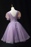 A lavender purple tulle dress displayed on a white mannequin against a black background. The dress features a lace-up open back, sheer puff sleeves, and a sparkly tulle skirt.