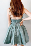 A woman shown from the back wearing a short, sparkly metallic teal-green spaghetti-strap dress against a plain light gray background.