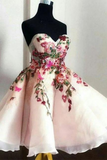 A strapless sweetheart ball gown with a voluminous tulle skirt, featuring vibrant pink, red, and green floral embroidery and applique on a black dress form.