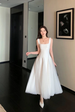 Woman in a white dress standing in a room with a mirror and framed picture on the wall.