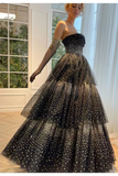 A woman models a strapless black tulle ball gown with sheer long sleeves and dense silver rhinestone embellishments, set in a bright indoor room with large windows and white curtains.