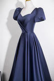 A navy blue satin A-line gown with puffed short sleeves, a sweetheart neckline, and a wrap-style bodice, displayed on a mannequin against a plain white wall.