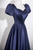 A navy blue satin dress displayed on a white mannequin against a plain light background. The dress features a sweetheart neckline, puffed short sleeves, a fitted corset-style bodice, and a full skirt.