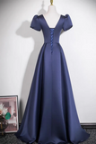 A floor-length navy blue satin gown displayed on a mannequin against a plain white wall. The dress has short puff sleeves, a deep V-neckline, and lace-up detailing at the bodice.