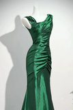 A floor-length emerald green satin gown with a draped, ruched bodice and one-shoulder neckline, displayed on a white mannequin against a plain light background.